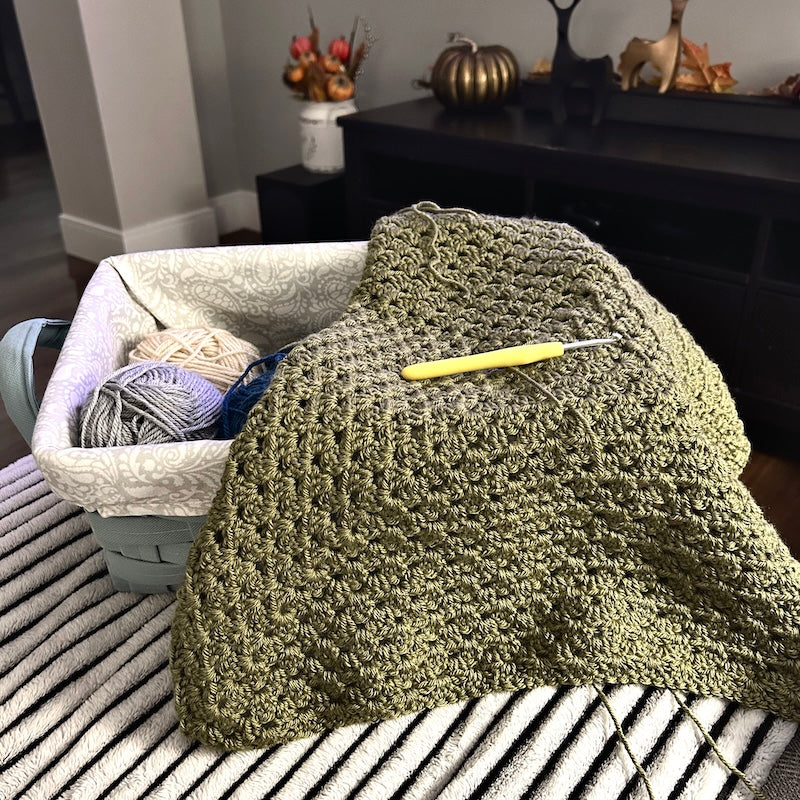 A crocheted blanket laying over a basket of yarn from the granny square blanket kit.