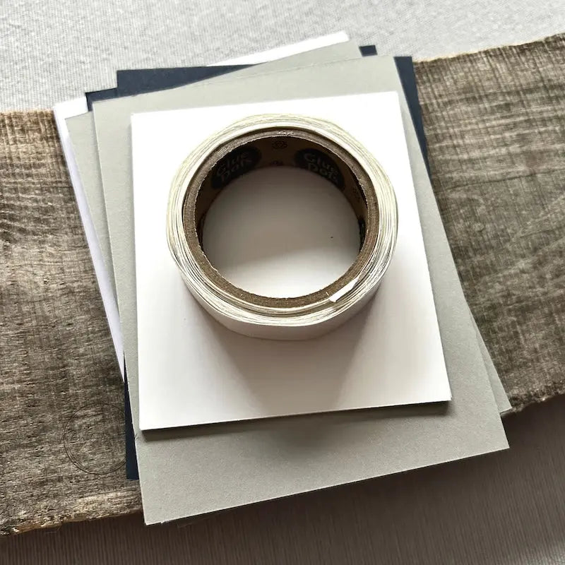 A roll of glue dots and a sheet of pop dots are sitting on a few blank cards. They are included in your card making kit.