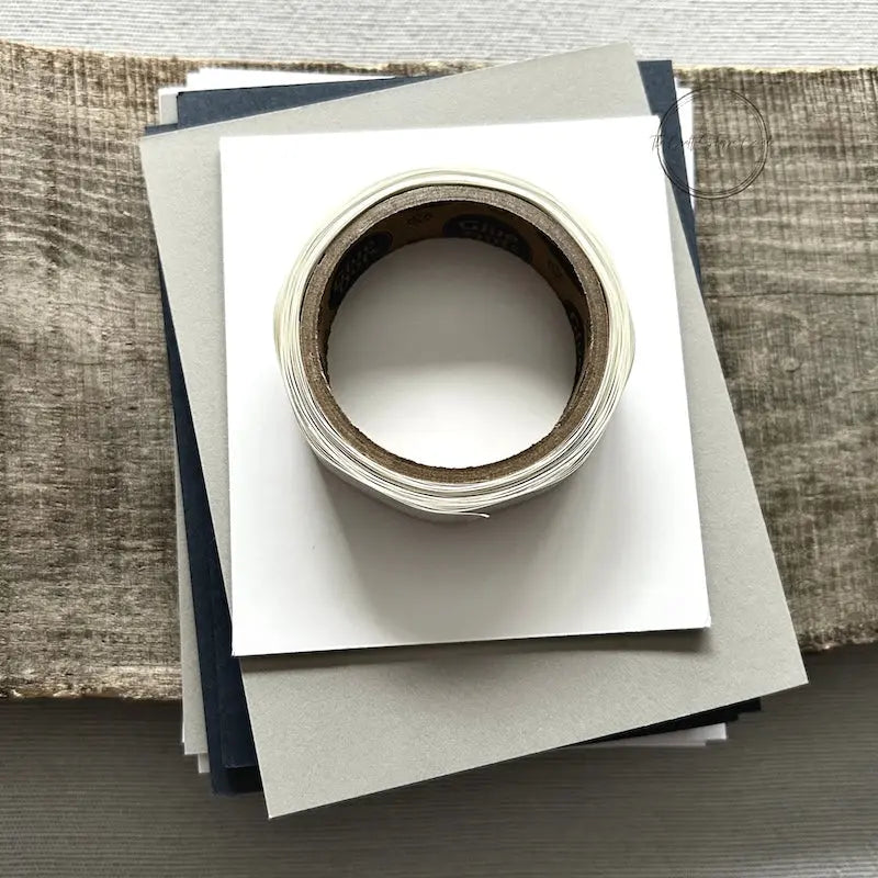 A roll of glue dots and a sheet of pop dots are sitting on a few blank cards. They are included in your card making kit.