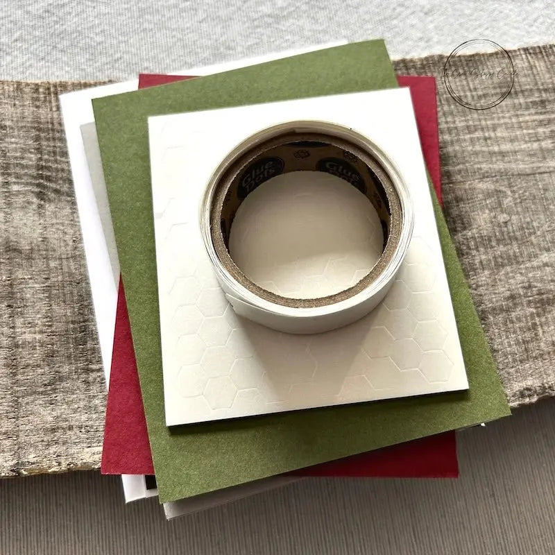 A roll of glue dots and a sheet of pop dots are sitting on a few blank cards. They are included in your card making kit.