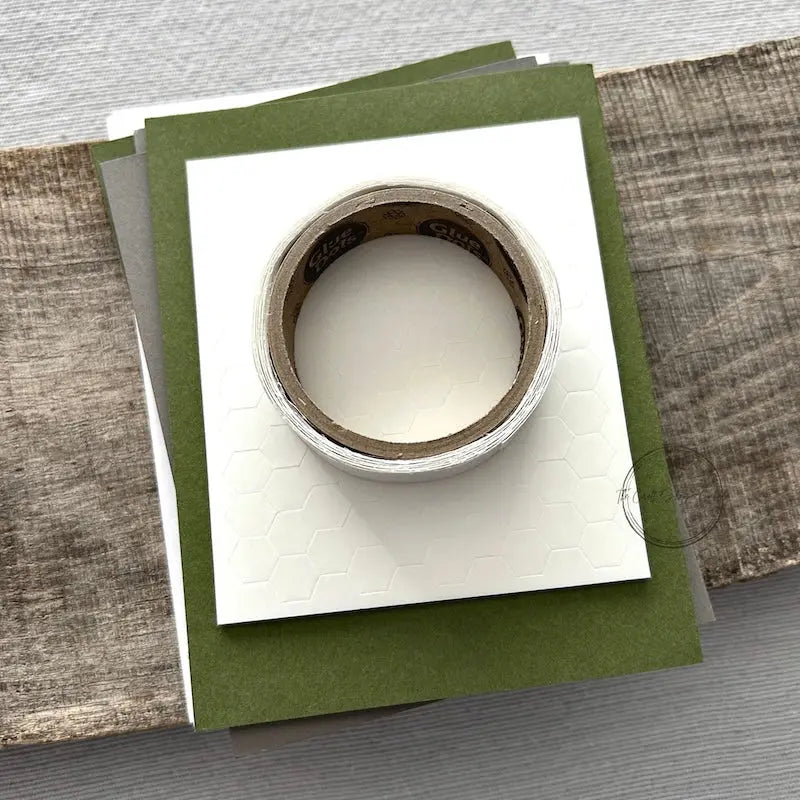 A roll of glue dots and a sheet of pop dots are sitting on a few blank cards. They are included in your card making kit.