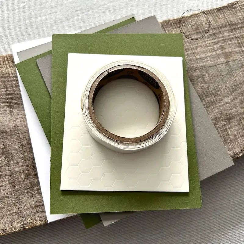 A roll of glue dots and a sheet of pop dots are sitting on a few blank cards. They are included in your card making kit.