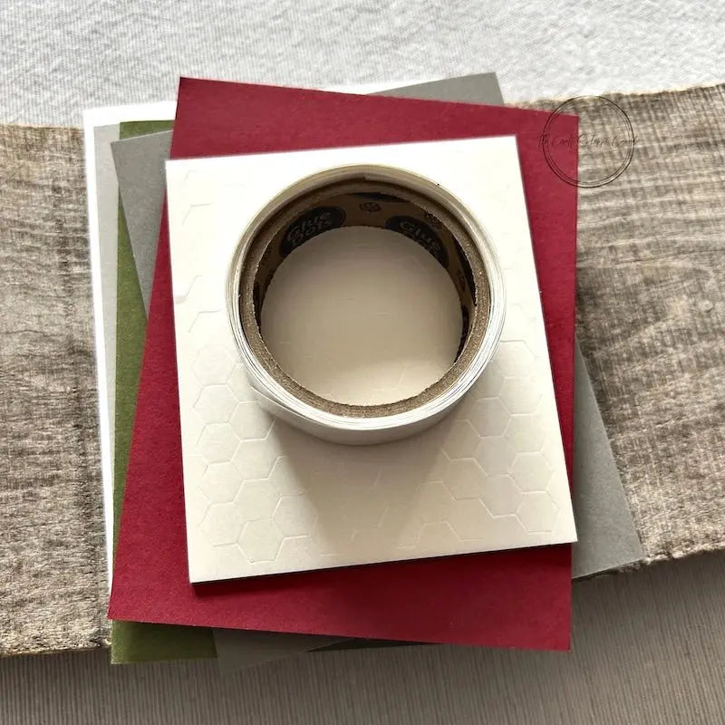 A roll of glue dots and a sheet of pop dots are sitting on a few blank cards. They are included in your card making kit.