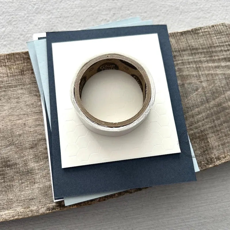 A roll of glue dots and a sheet of pop dots are sitting on a few blank cards. They are included in your card making kit.