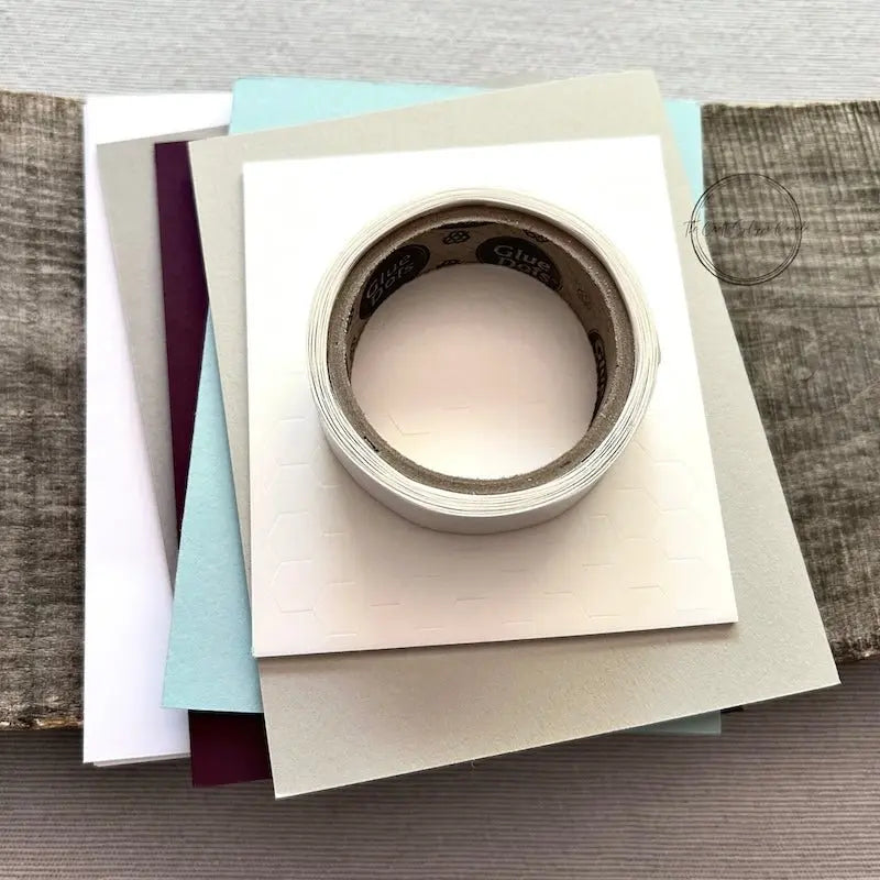 A roll of glue dots and a sheet of pop dots are sitting on a few blank cards. They are included in your card making kit.