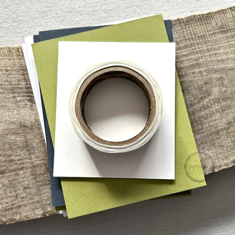 A roll of glue dots and a sheet of pop dots are sitting on a few blank cards. They are included in your card making kit.