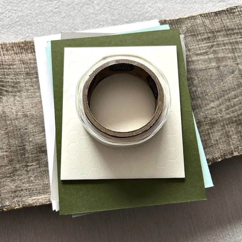 A roll of glue dots and a sheet of pop dots are sitting on a few blank cards. They are included in your card making kit.