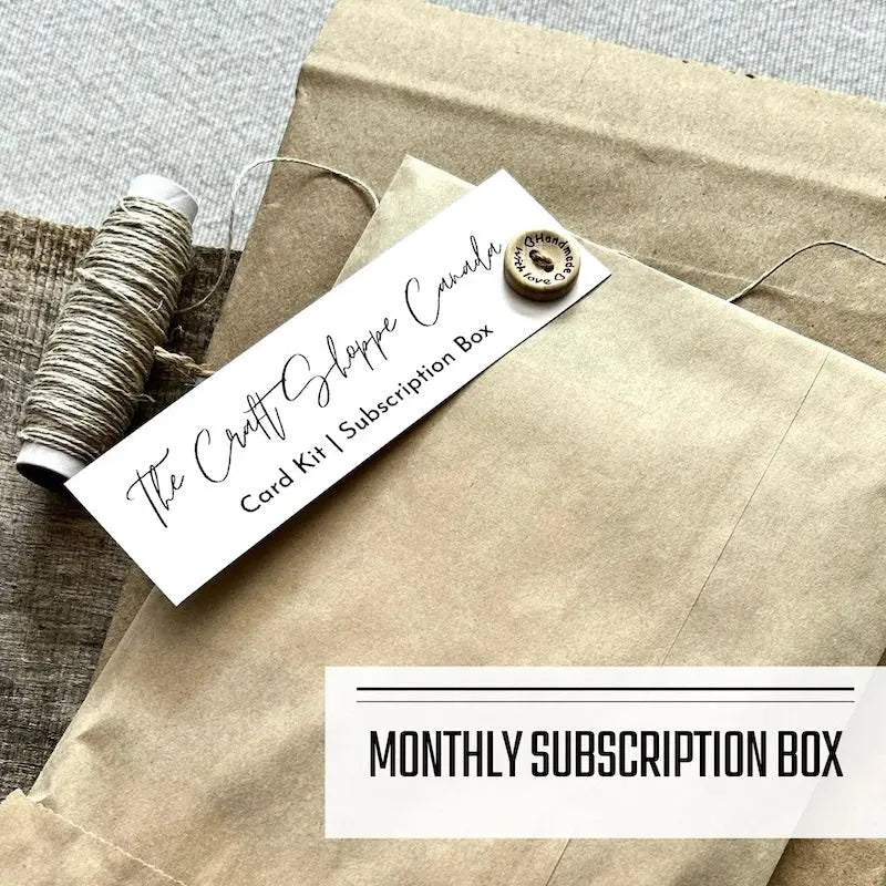 A monthly subscription box program featuring DIY card making kits. A subscription box envelope is sitting on a wooden board with a roll of twine.