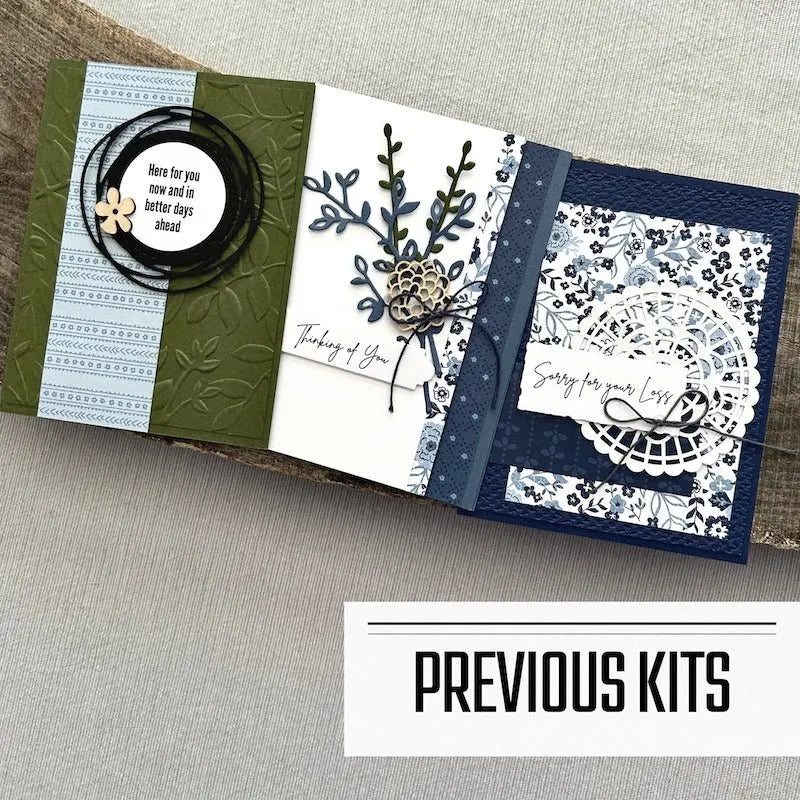 There are 3 finished cards, sitting on a wooden board, to show what cards have been sent in previous kits.