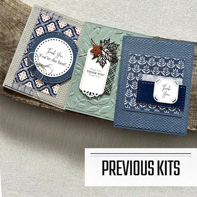 There are 3 finished cards, sitting on a wooden board, to show what cards have been sent in previous kits.