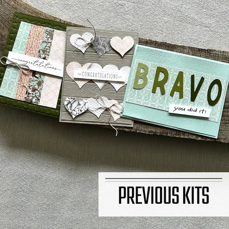 There are 3 finished cards, sitting on a wooden board, to show what cards have been sent in previous kits.