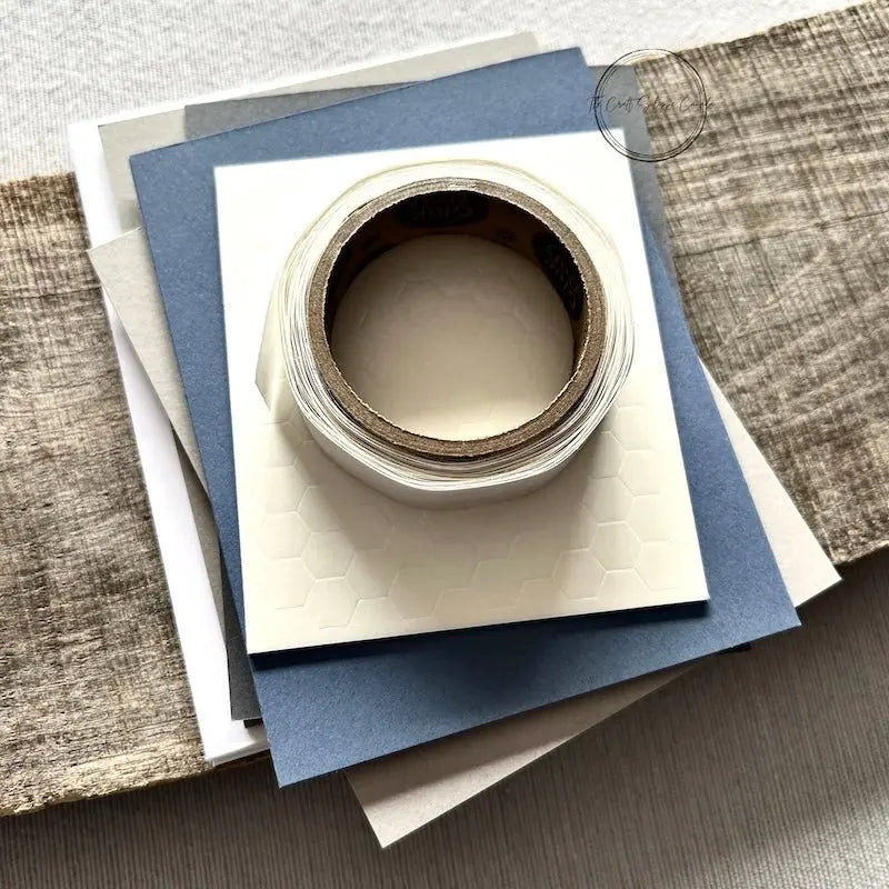 A roll of glue dots and a sheet of pop dots are sitting on a few blank cards. They are included in your card making kit.