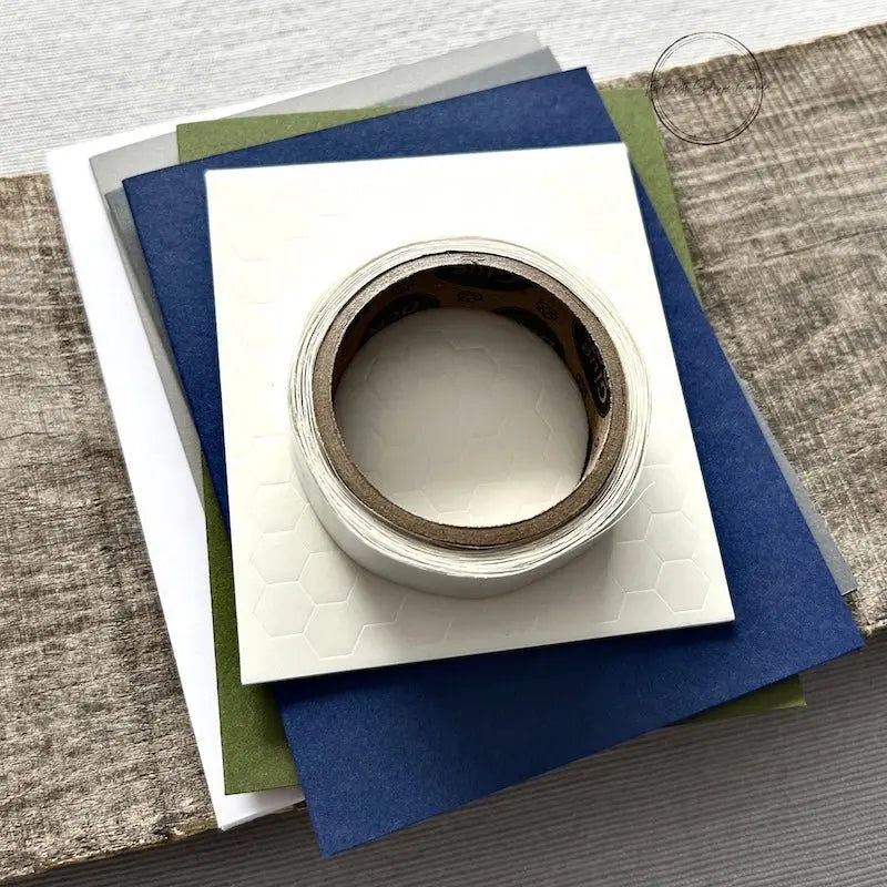 A roll of glue dots and a sheet of pop dots are sitting on a few blank cards. They are included in your card making kit.