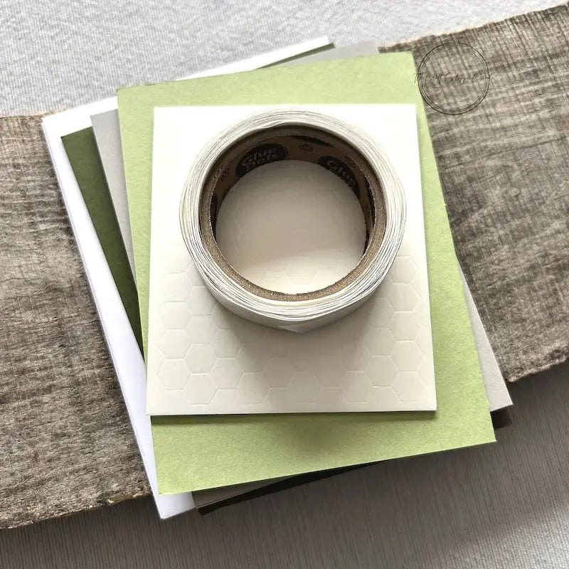 A roll of glue dots and a sheet of pop dots are sitting on a few blank cards. They are included in your card making kit.