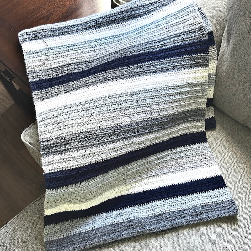 The finished couch throw, made from this crochet kit, is draped over a couch.