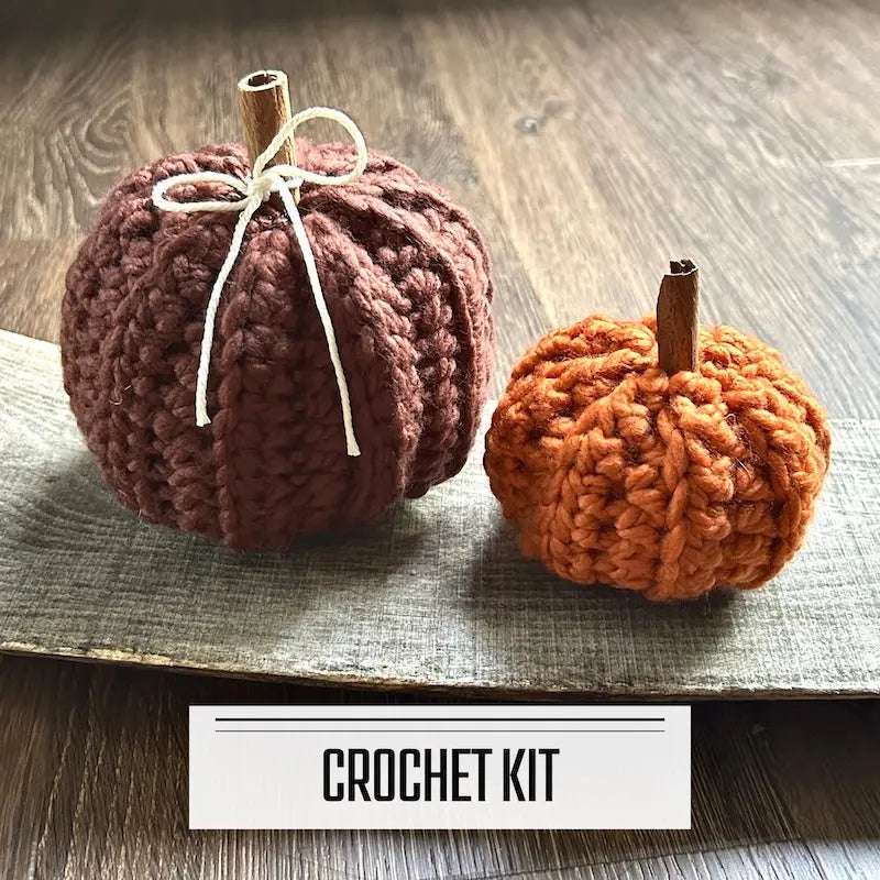A crochet kit for a set of autumn pumpkins. The finished pumpkins are sitting on a wooden board.