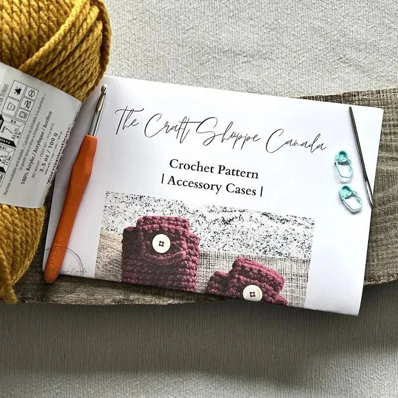 The pattern for this crochet kit is lying on a wooden board with yarn, a crochet hook, a tapestry needle and 2 stitch markers.