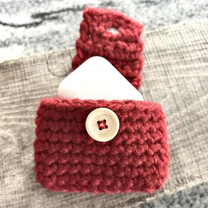The finished ear buds case, from this crochet kit, is sitting on a wooden board with a pair of ear buds poking out from the top.