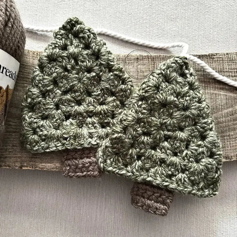 2 of the Christmas trees, made from this crochet pattern, are sitting on a wooden board.