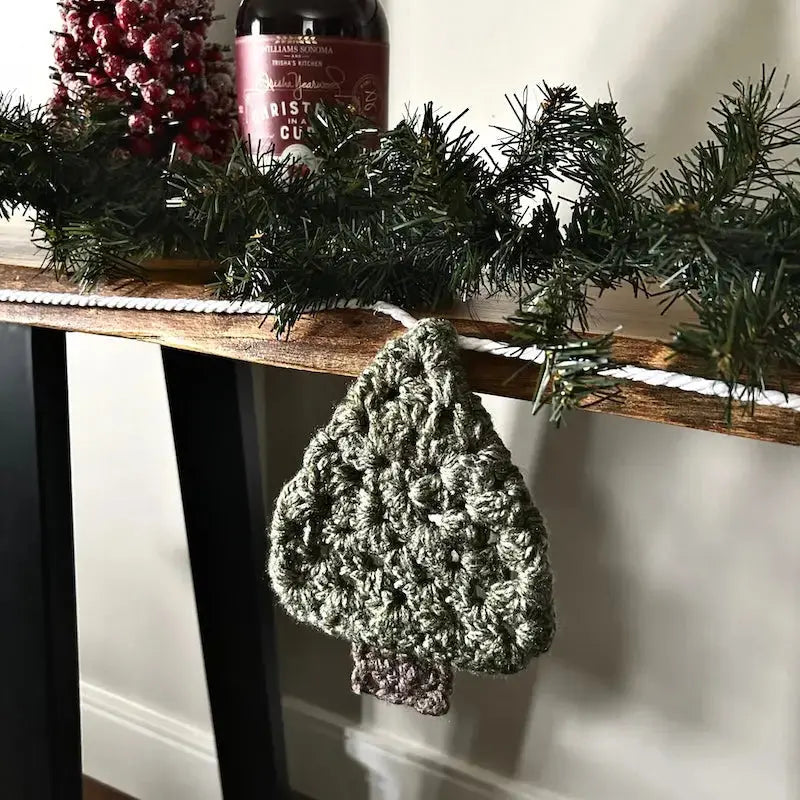 The Christmas garland, made from this crochet pattern, is hanging off of a table with Christmas decorations behind it.
