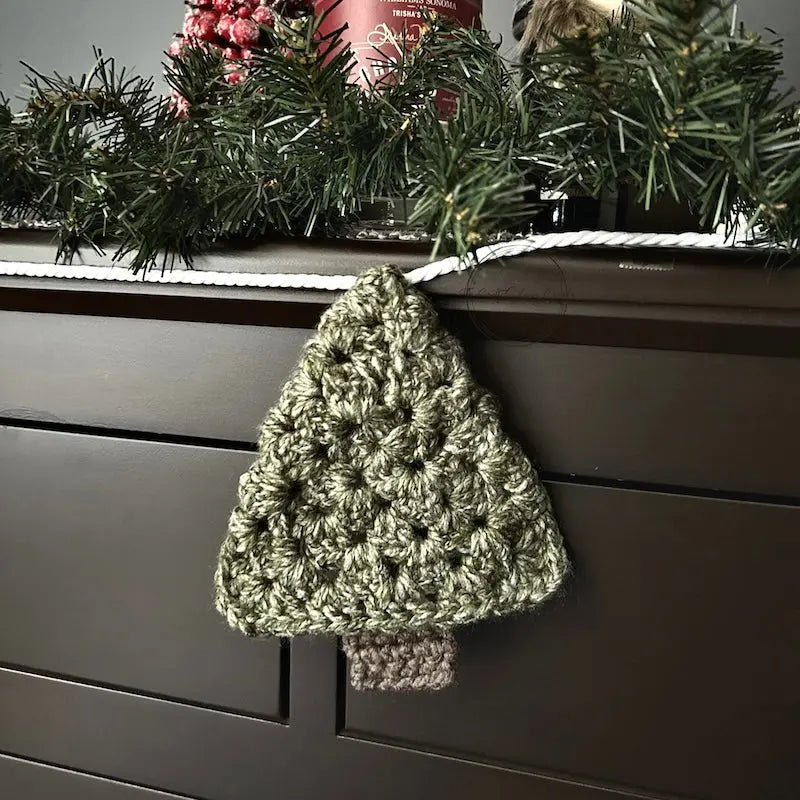 The Christmas garland, made from this crochet pattern, is hanging off of a buffet with Christmas decorations behind it.