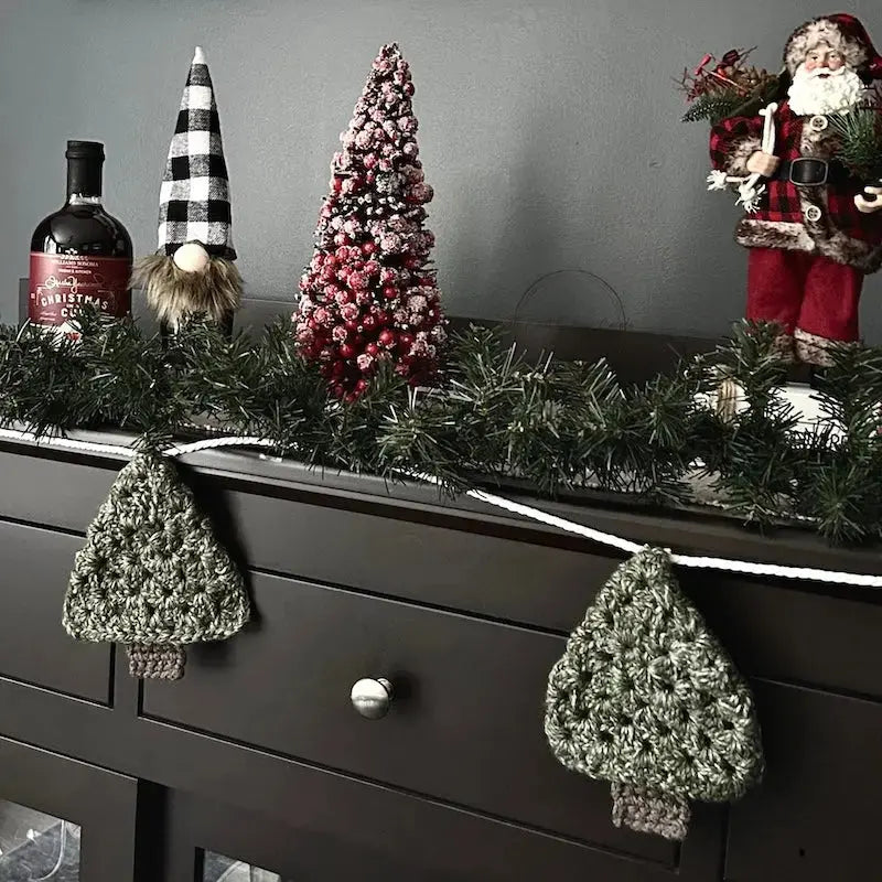 The Christmas garland, made from this crochet pattern, is hanging off of a buffet with Christmas decorations behind it.