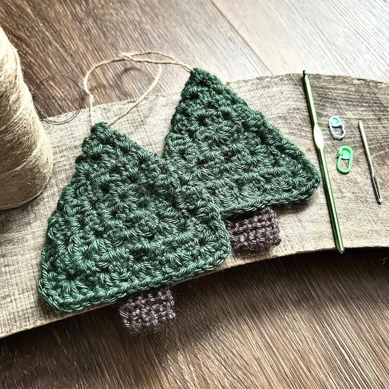 2 green Christmas tree ornaments, made from this crochet kit, are sitting on a wooden board.