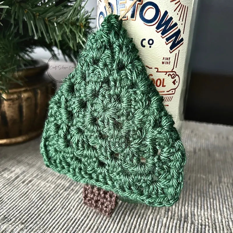 A finished Christmas tree ornament, made from this crochet kit, is hanging from a bottle of wine.
