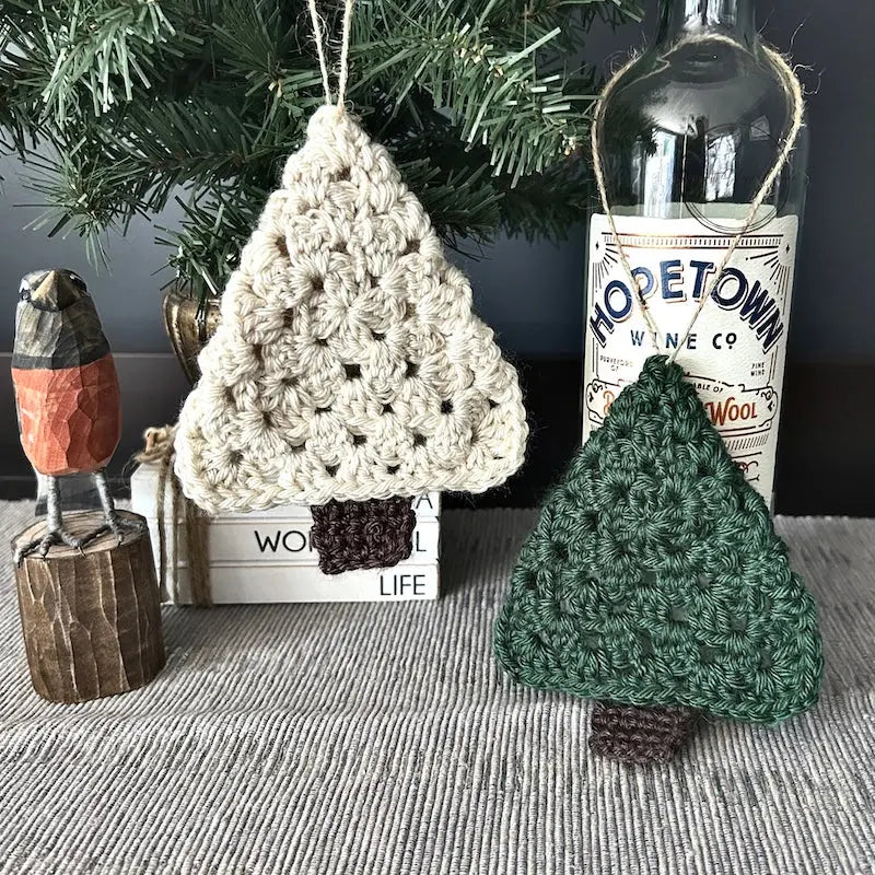 The Christmas tree ornaments, made from this crochet kit, are hanging from a tree that is sitting on a buffet.