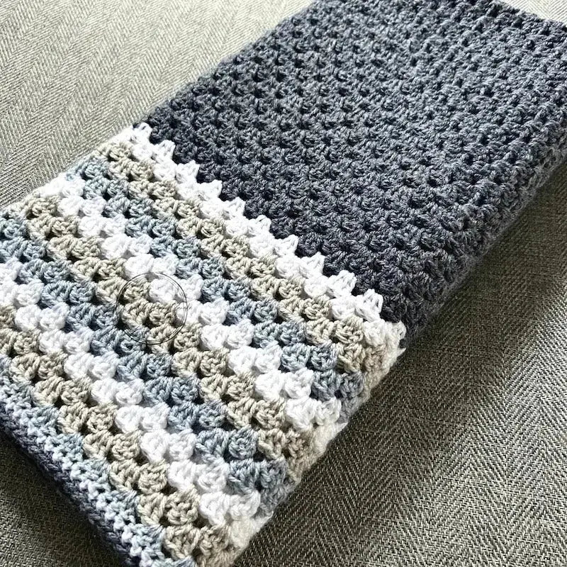 The finished granny square blanket, made from this crochet kit, is lying across a couch.