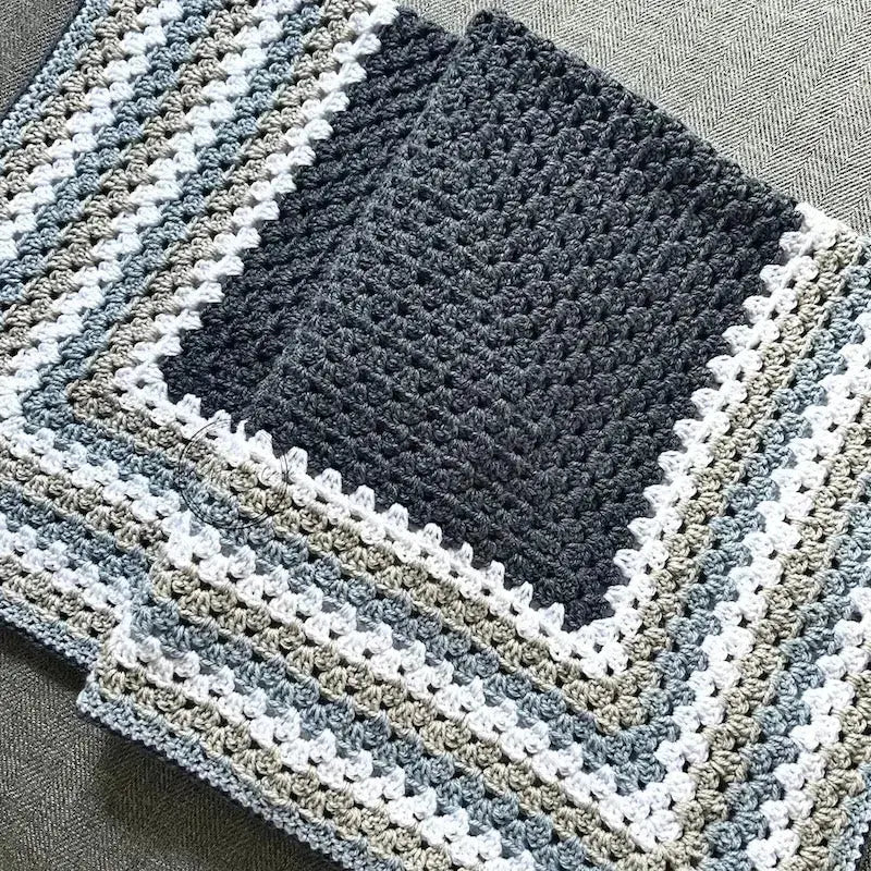 The finished granny square blanket, made from this crochet pattern, is lying across a couch.