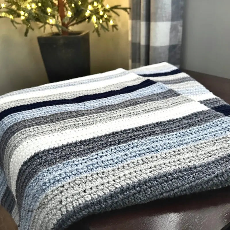 The finished couch throw, made from this crochet kit, is draped over a table with Christmas lights.