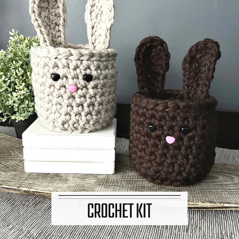 A DIY crochet kit for an Easter bunny basket set. The finished baskets are sitting on a wooden board with a plant.