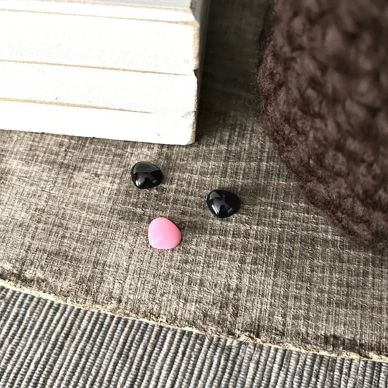 The eyes and nose that are included in this crochet kit are sitting on a wooden board.