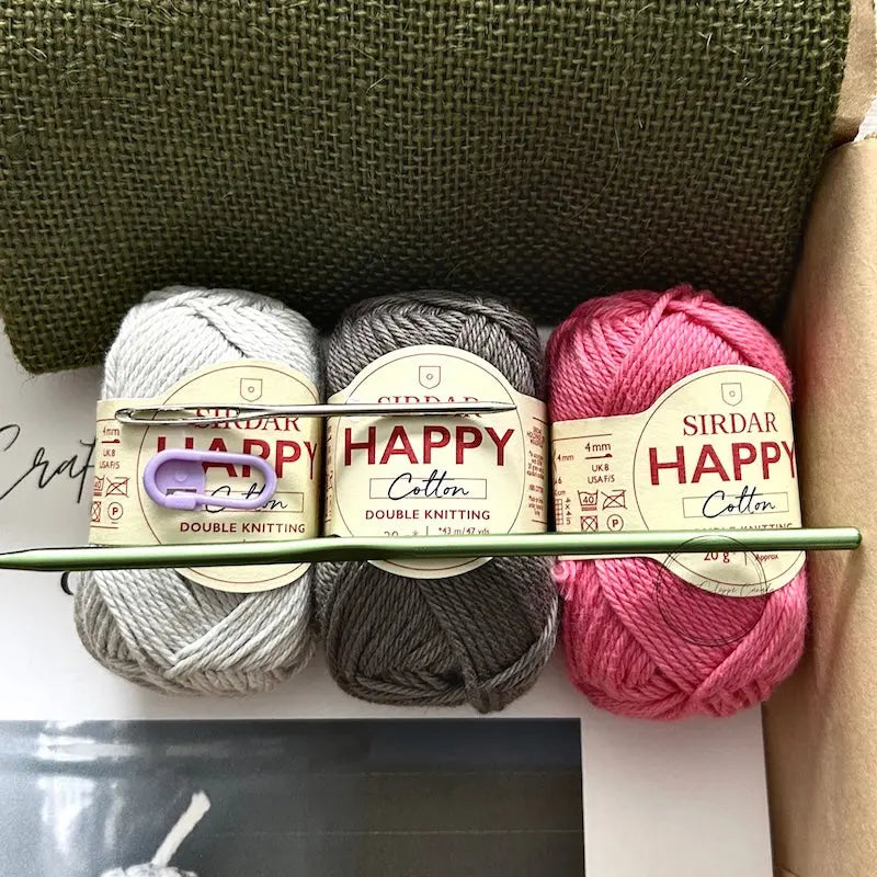 The yarn used in this crochet pattern is lying in a box with a crochet hook, stitch marker and a tapestry needle.