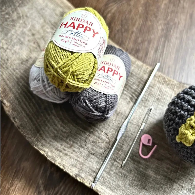 The yarn, used in this crochet kit is sitting on a wooden board with a crochet hook.