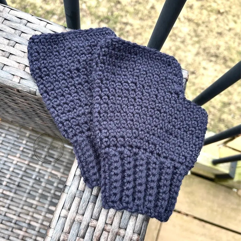 The finished mittens, made from this crochet kit, are lying on the edge of patio furniture.