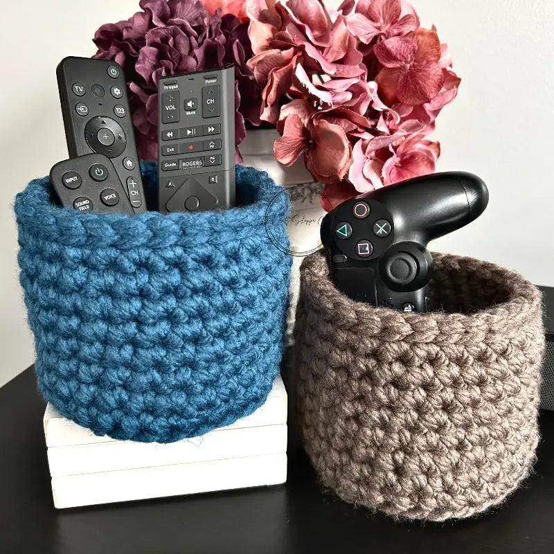 The storage baskets, from this crochet kit, are sitting on a wooden table with TV and game remotes in the baskets.