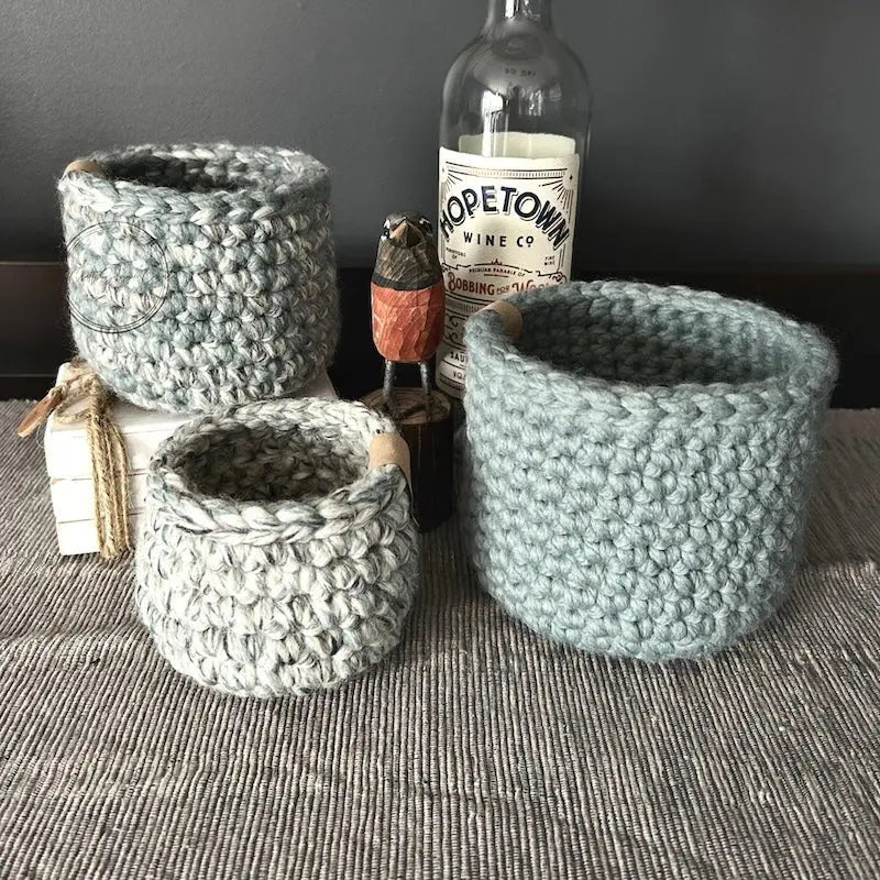 The 3 storage baskets, from this crochet kit, on top of a buffet with spring decor.