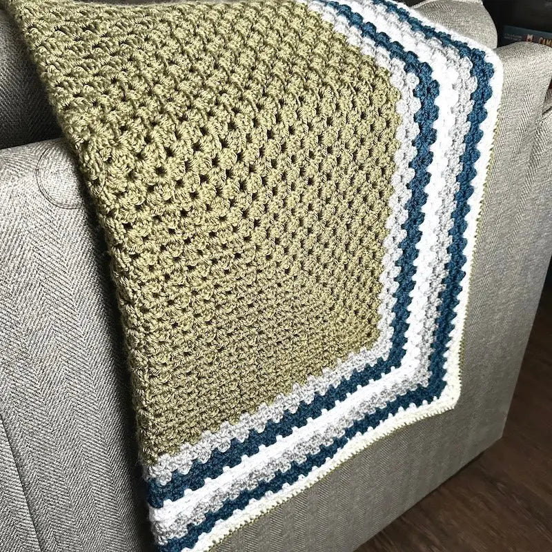 The finished granny square blanket, from this crochet kit, is lying across a couch.