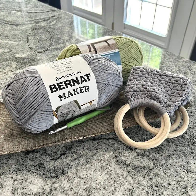 The towel holders, from this crochet kit, are folded on a wooden board with yarn and a crochet hook.