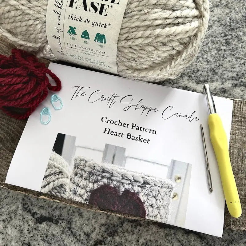 A close up of the pattern, from this crochet kit, lying on a wooden board with yarn, a crochet hook, and a tapestry needle.
