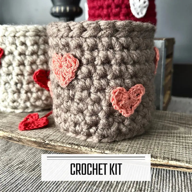 A DIY crochet kit for a Valentine heart basket. The finished baskets are sitting on a wooden board.