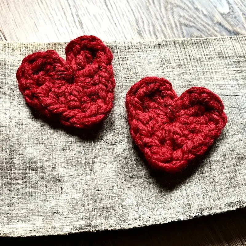 Red crocheted hearts, made from this crochet pattern, are sitting on a wooden board.
