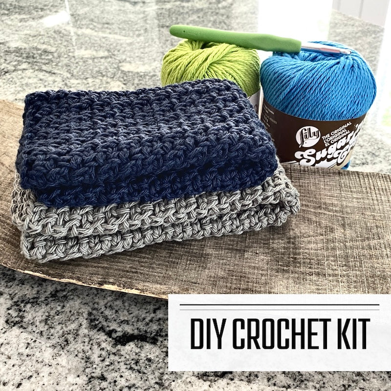 A DIY crochet kit for a dishcloth washcloth. The washcloths are sitting on a wooden board with yarn and a crochet hook.
