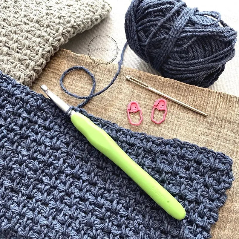 The blue and grey dishcloths, from this crochet kit, along with yarn, a tapestry needle, stitch markers and a crochet hook.