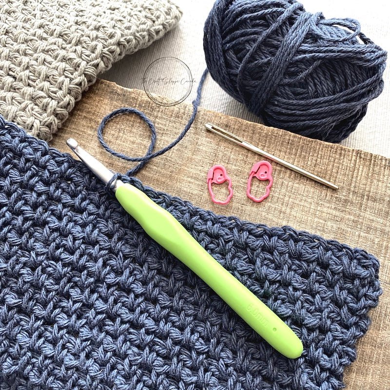 The blue and grey dishcloths, from this crochet kit, along with yarn, a tapestry needle, stitch markers and a crochet hook.