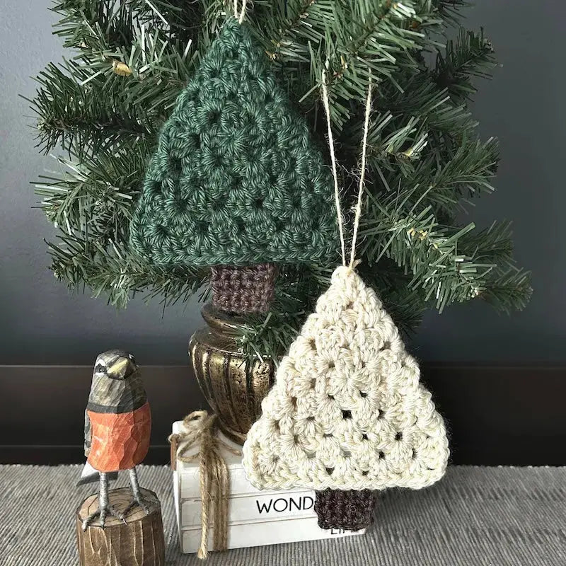 The Christmas tree ornaments, made from this crochet pattern, are hanging from a tree that is sitting on a buffet.