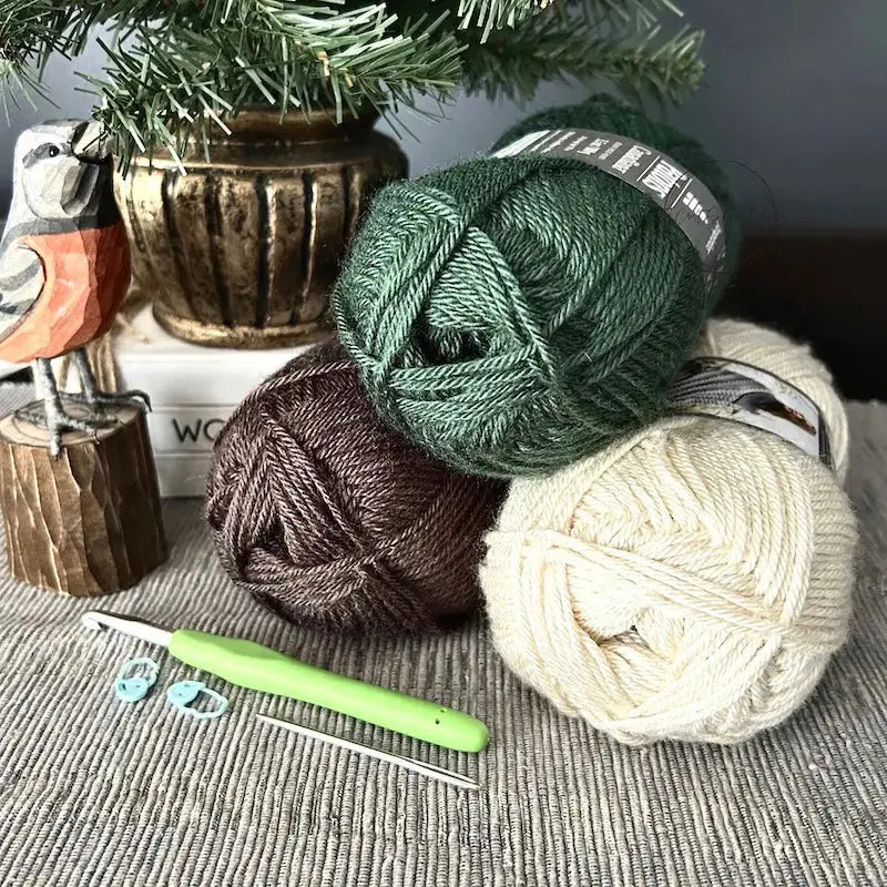 The yarn, that would be used for this crochet pattern, is sitting on a buffet with a crochet hook, a tapestry needle and 2 stitch markers.