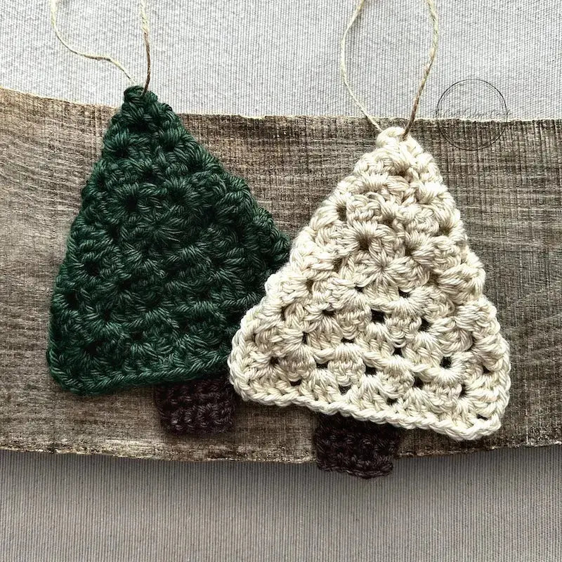 A green and ivory Christmas tree ornament, made from this crochet kit, are sitting on a wooden board.